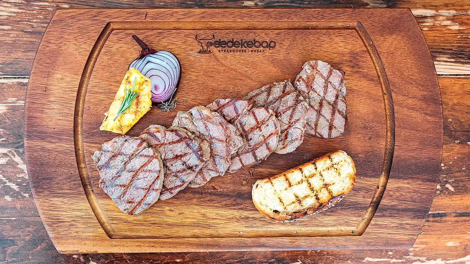 Kömür ateşinde ızgara edilmiş dana lokum dilimleri, közlenmiş ananas ve kırmızı soğan eşliğinde ahşap tahtada servis – Adana Dede Kebap Steak Burger Tatlı Kasap