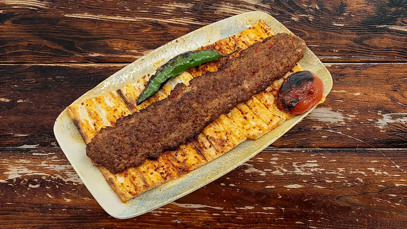 Kömür ateşinde közde pişirilmiş acılı Adana Kebap şiş, yanında közlenmiş domates, biber ve sıcak pide ile porsiyon sunum – Adana Dede Kebap Steak Burger Tatlı Kasap